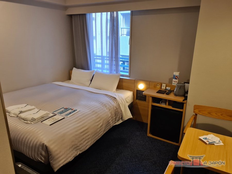 Habitación doble de un hotel de negocios japonés con cama grande, toallas dobladas sobre la cama y una ventana.