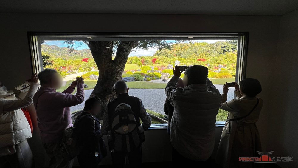Visitantes fotografiando el jardín enmarcado por una ventana del Museo de Arte Adachi