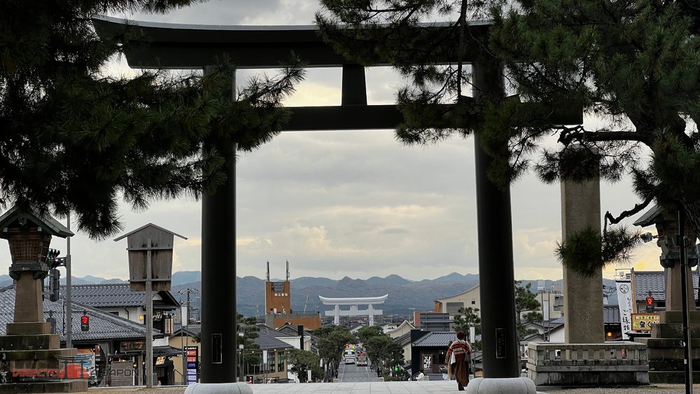 Torii oscuro de Izumo Taisha enmarcando Shinmon-dori y el gran torii blanco de Uga-bashi al fondo