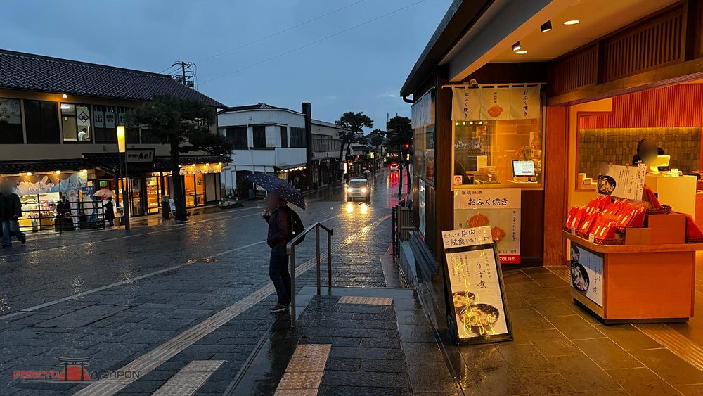 Calle comercial junto a Izumo Taisha al anochecer, con lluvia y tiendas iluminadas