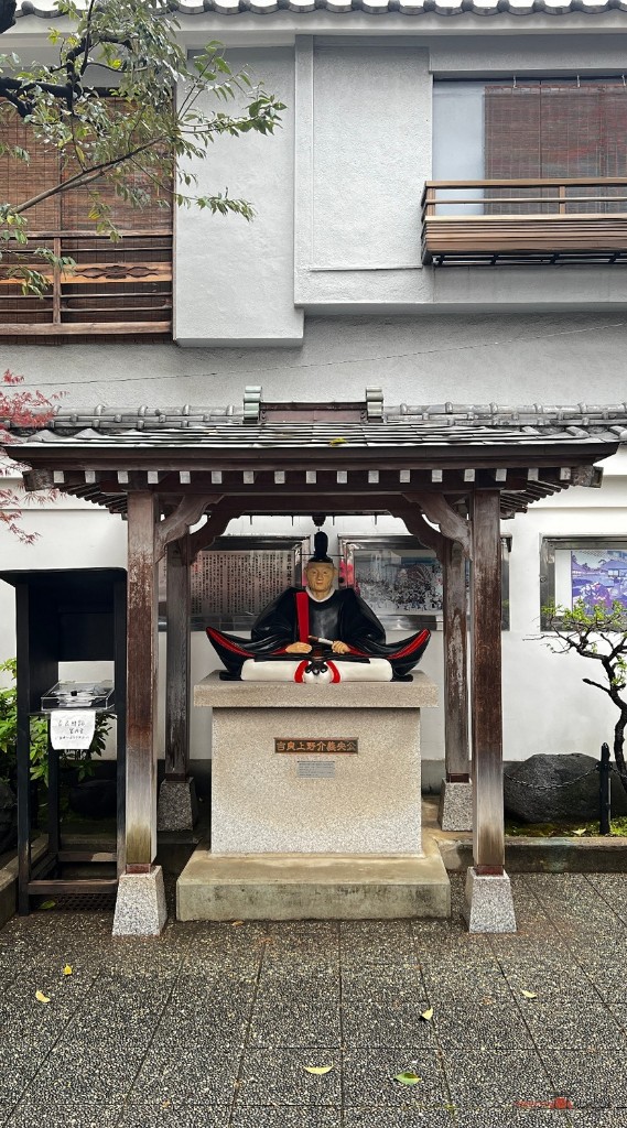 Estatua sentada de Kira Yoshinaka bajo un tejadillo