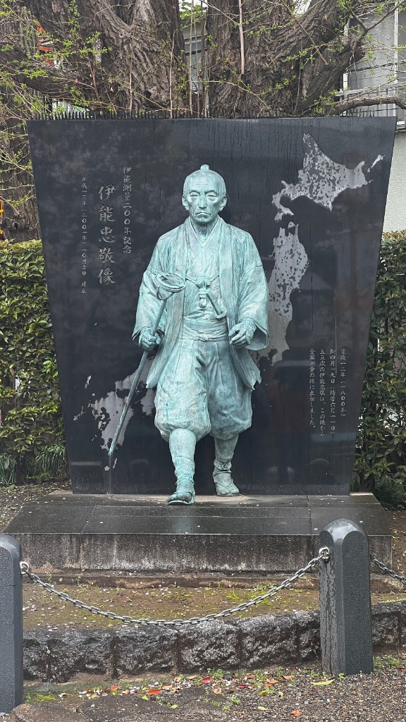 Estatua de bronce de Ino Tadataka sobre un panel de granito negro con el mapa de Japón, junto al santuario Tomioka Hachimangu.