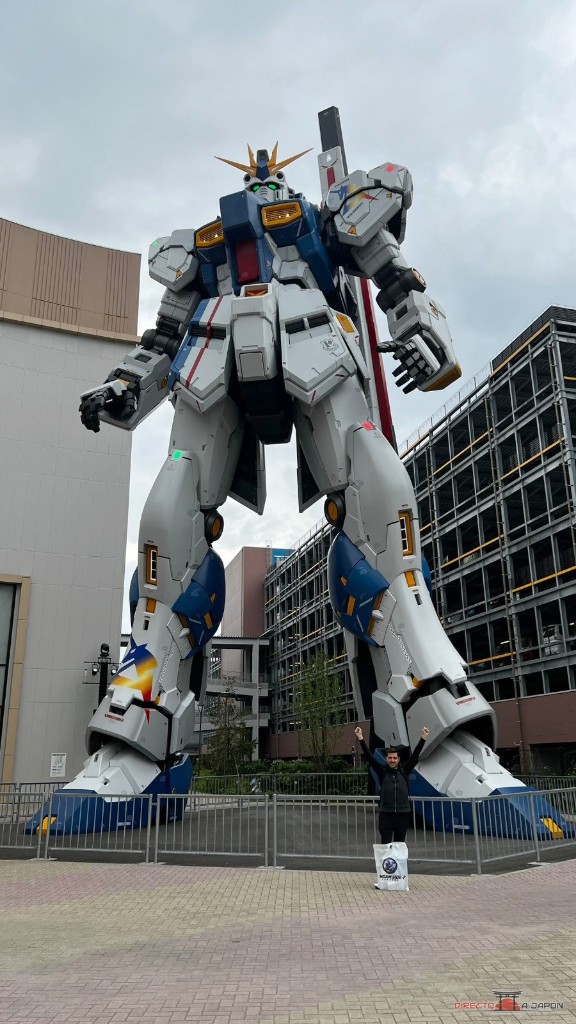 Edu con los brazos levantados ante el RX-93ffν Gundam de LaLaport Fukuoka.