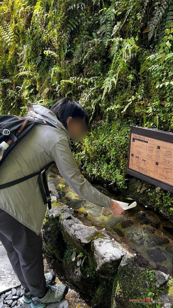 Visitante mojando su papel de la fortuna en la fuente de Kifune