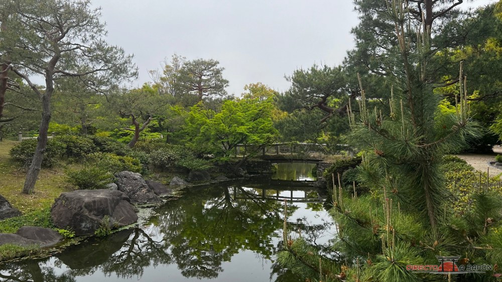 Canal de agua, pequeño puente y pinos en el Jardín Shirotori