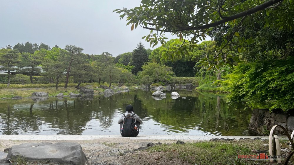 Visitante sentada de espaldas frente al estanque del Jardín Shirotori