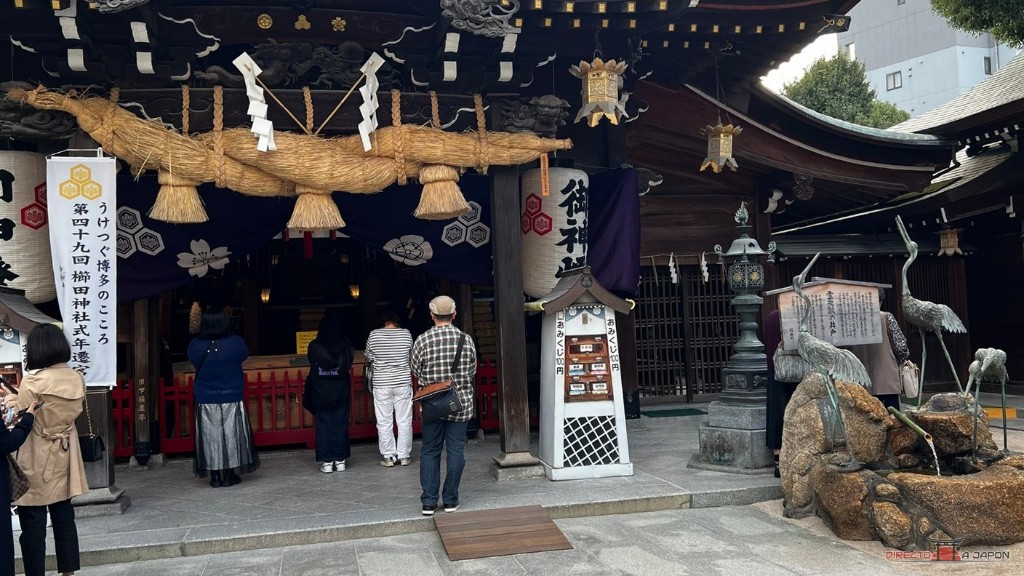 Pabellón de oración del santuario Kushida de Fukuoka con su gran shimenawa y, a la derecha, la fuente de las tres grullas de bronce