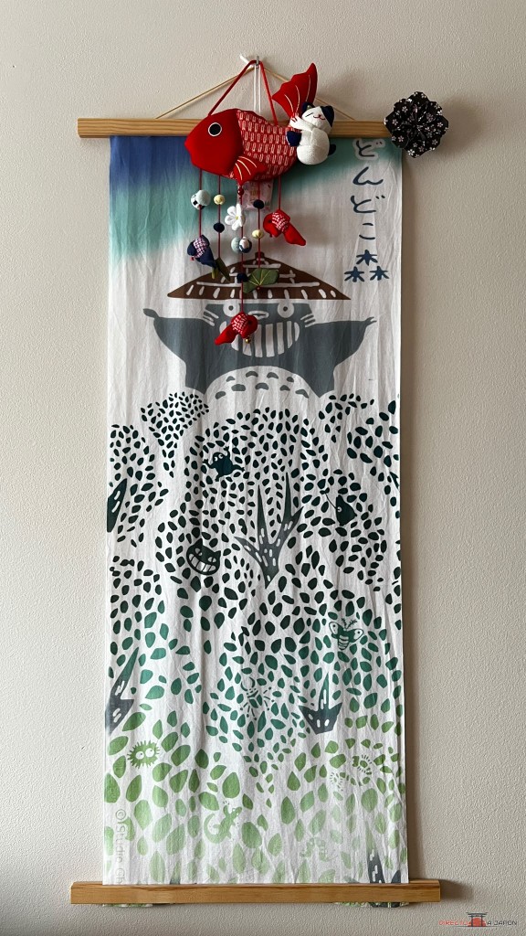 Tenugui de tela con motivos de Totoro comprado en el Parque Ghibli, colgado en casa con un colgante de tela