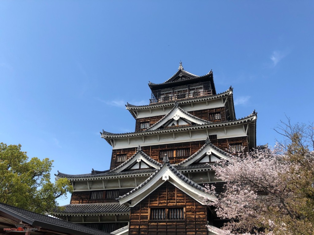 Torre principal del castillo de Hiroshima con un cerezo en flor
