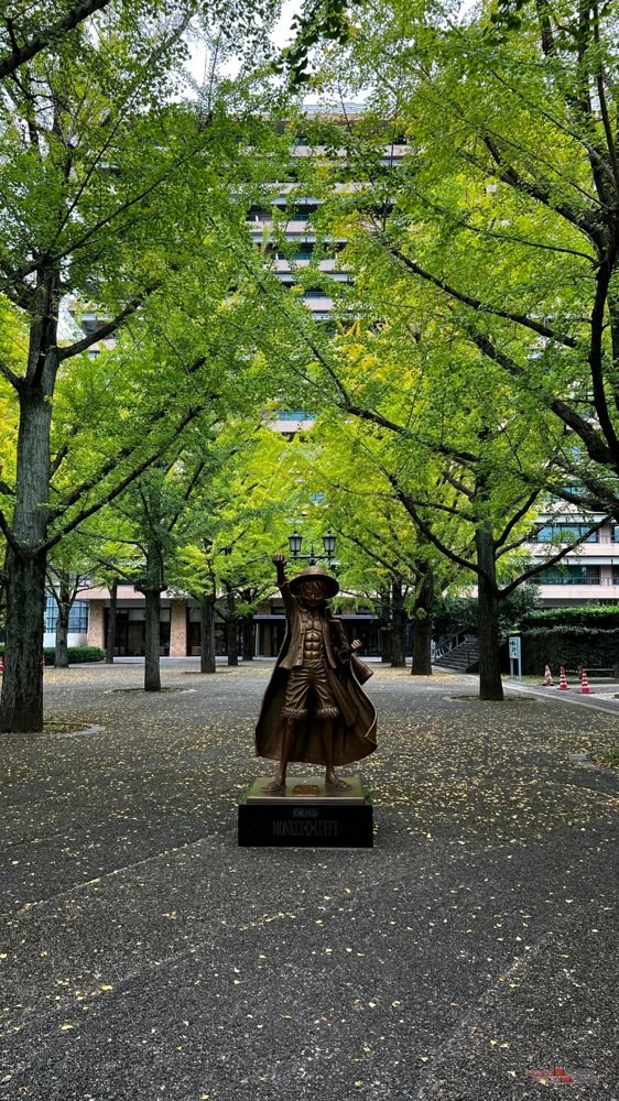 Estatua de Luffy entre ginkgos junto al edificio de la prefectura de Kumamoto