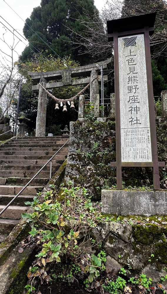 Cartel de piedra con el nombre del santuario y primer torii con escaleras detrás, junto a la carretera