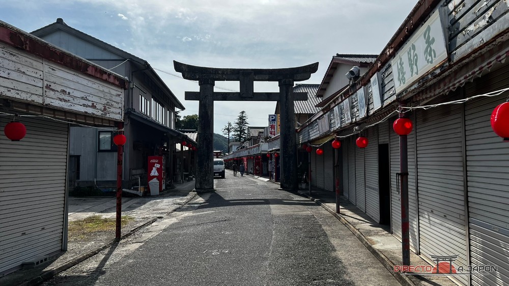 Calle comercial con tiendas cerradas y un torii de piedra al fondo, de camino al santuario Yutoku Jinja