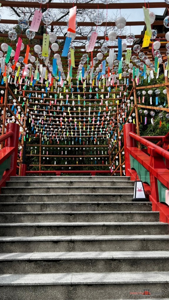 Escalera de piedra con barandillas rojas y cientos de campanillas de viento con tiras de papel colgadas encima