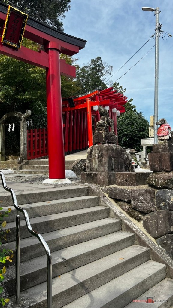 Torii rojo y escalera de piedra con pasamanos al inicio de la subida del santuario Yutoku Jinja