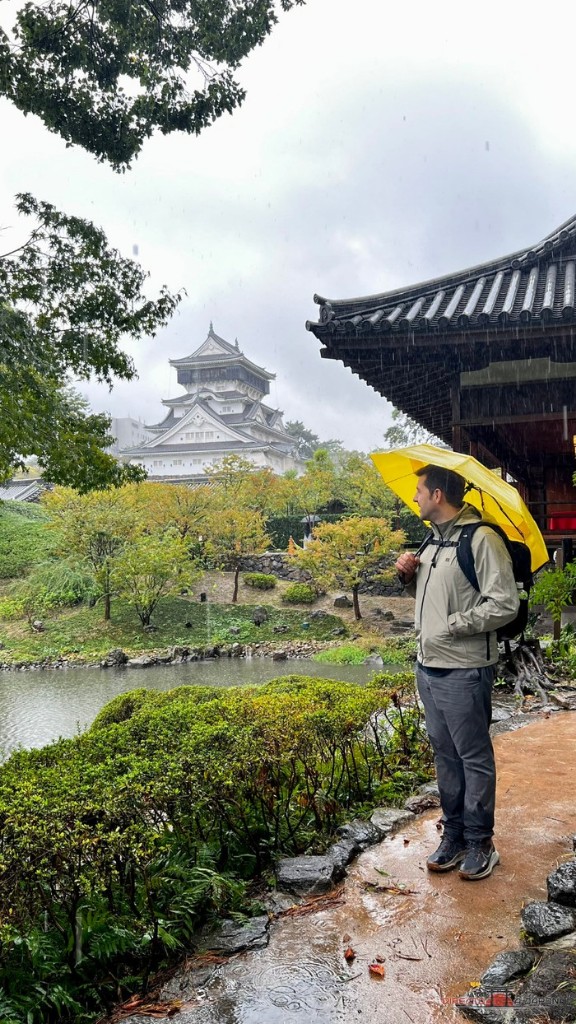 Edu con un paraguas amarillo en el jardín del castillo de Kokura, con la torre al fondo