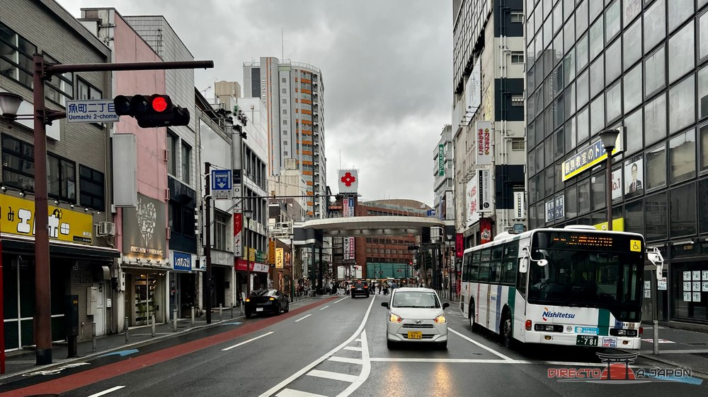 Calle de Uomachi, en el centro de Kokura, con autobús y edificios bajo un cielo gris