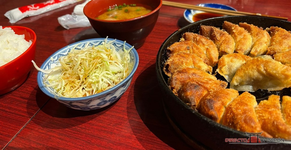 Gyozas en una plancha de hierro, con arroz, sopa y ensalada de col en una mesa de madera