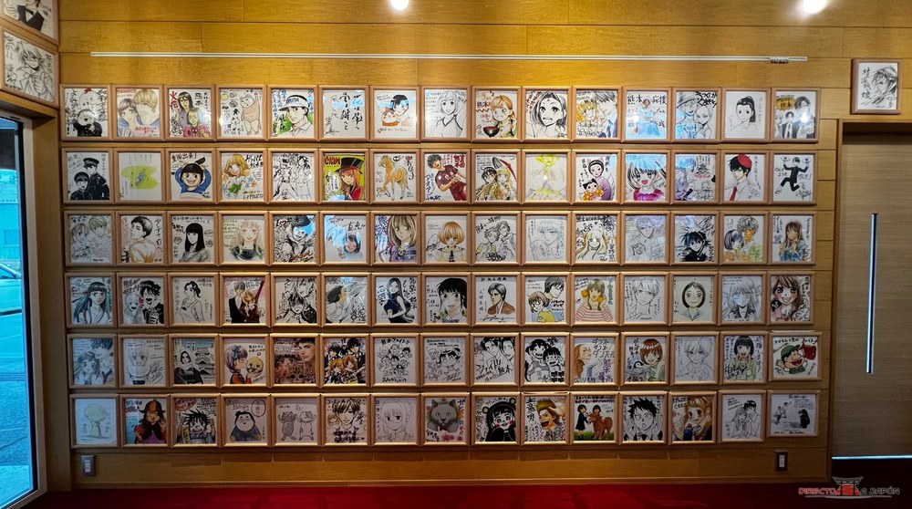 Pared de la estación de Takamori cubierta de dibujos de autores de manga enmarcados
